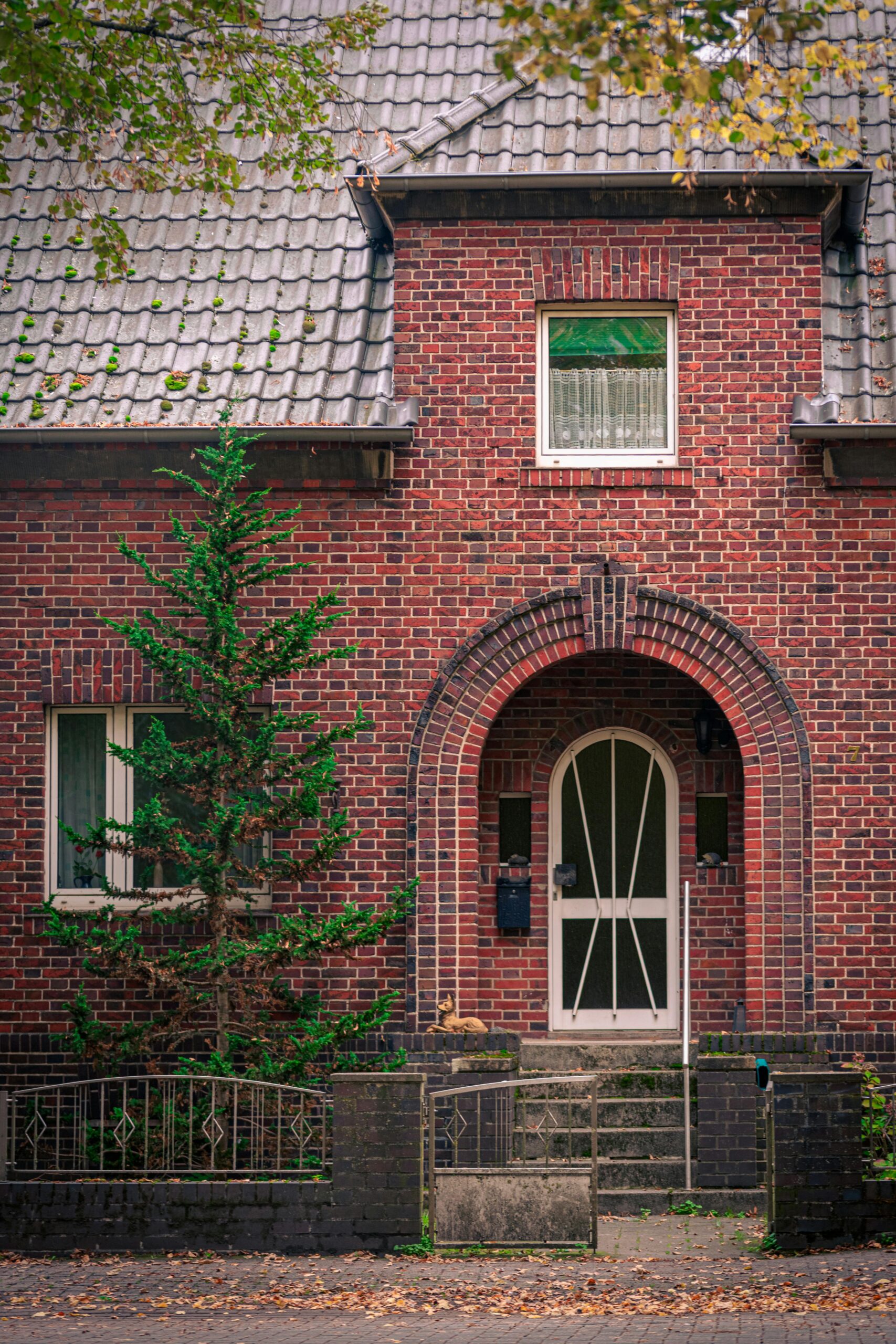 Cozy brick house with an arched doorway surrounded by greenery, perfect for real estate listings.